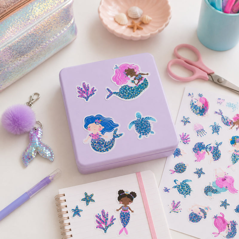 Decorative storage box personalised with mermaid stickers surrounded by stationery and craft supplies. Glitter details shimmer across the mermaids, sea turtles and coral pieces, creating an enchanting underwater display.
