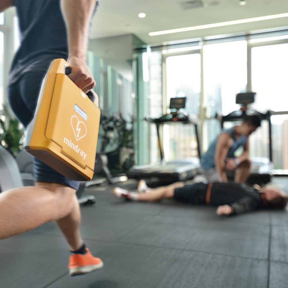 Person running with a Mindray C1A defibrillator towards a collapsed man in a gym
