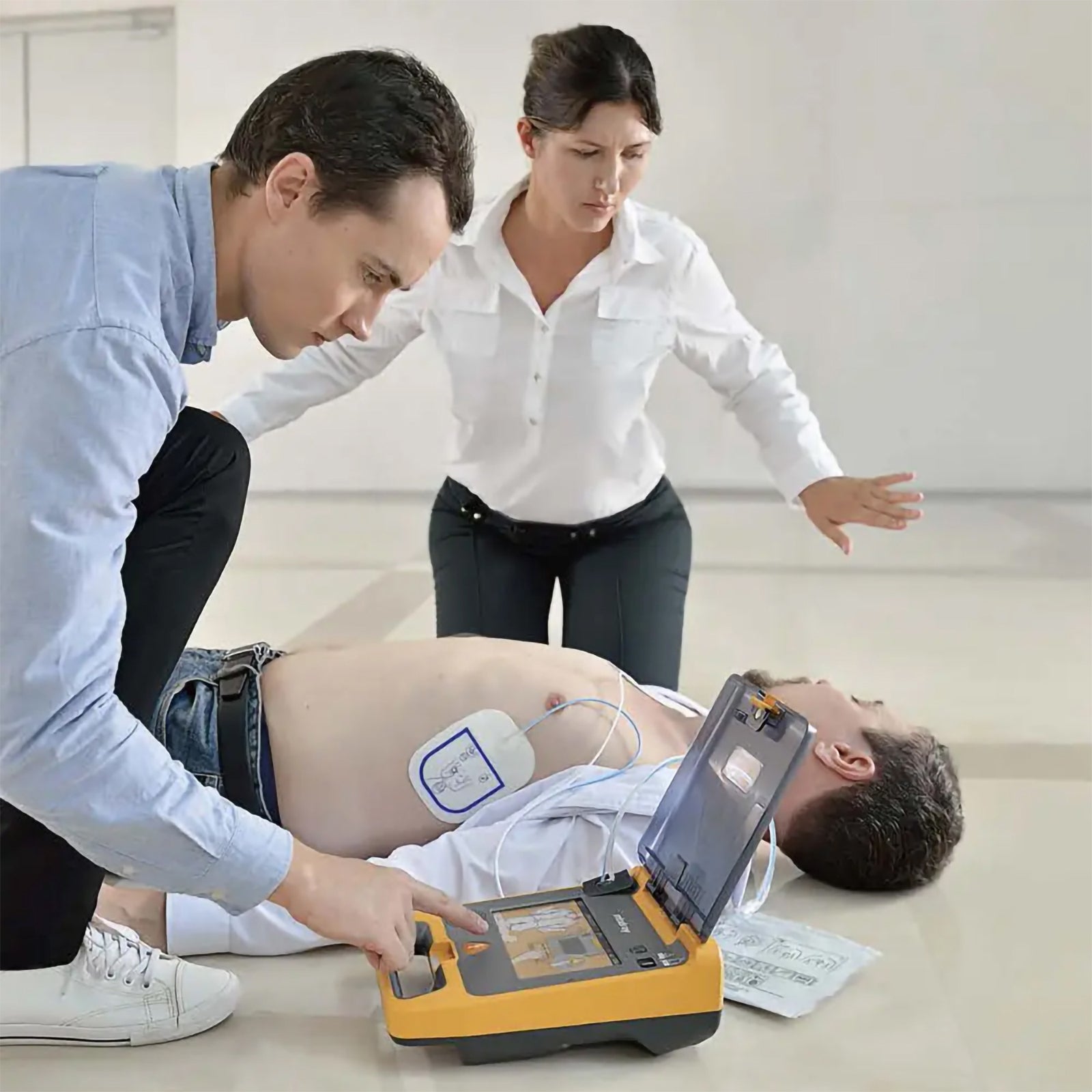 Mindray C2 Fully Automatic Defibrillator in use during a simulated emergency with electrode pads attached to an adult patient while two responders follow the device guidance and coordinate the cardiac arrest response.
