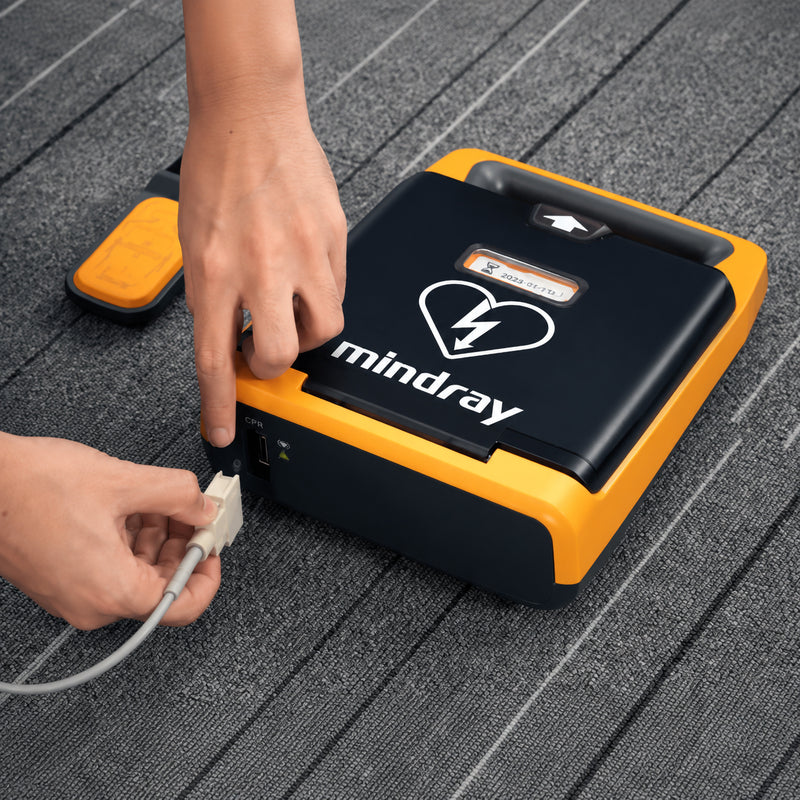 Mindray BeneHeart AED shown with its CPR sensor being connected to the dedicated CPR port. The close up training view demonstrates the wired sensor connection and compact AED design, helping users understand how the CPR feedback accessory integrates with a compatible Mindray defibrillator.
