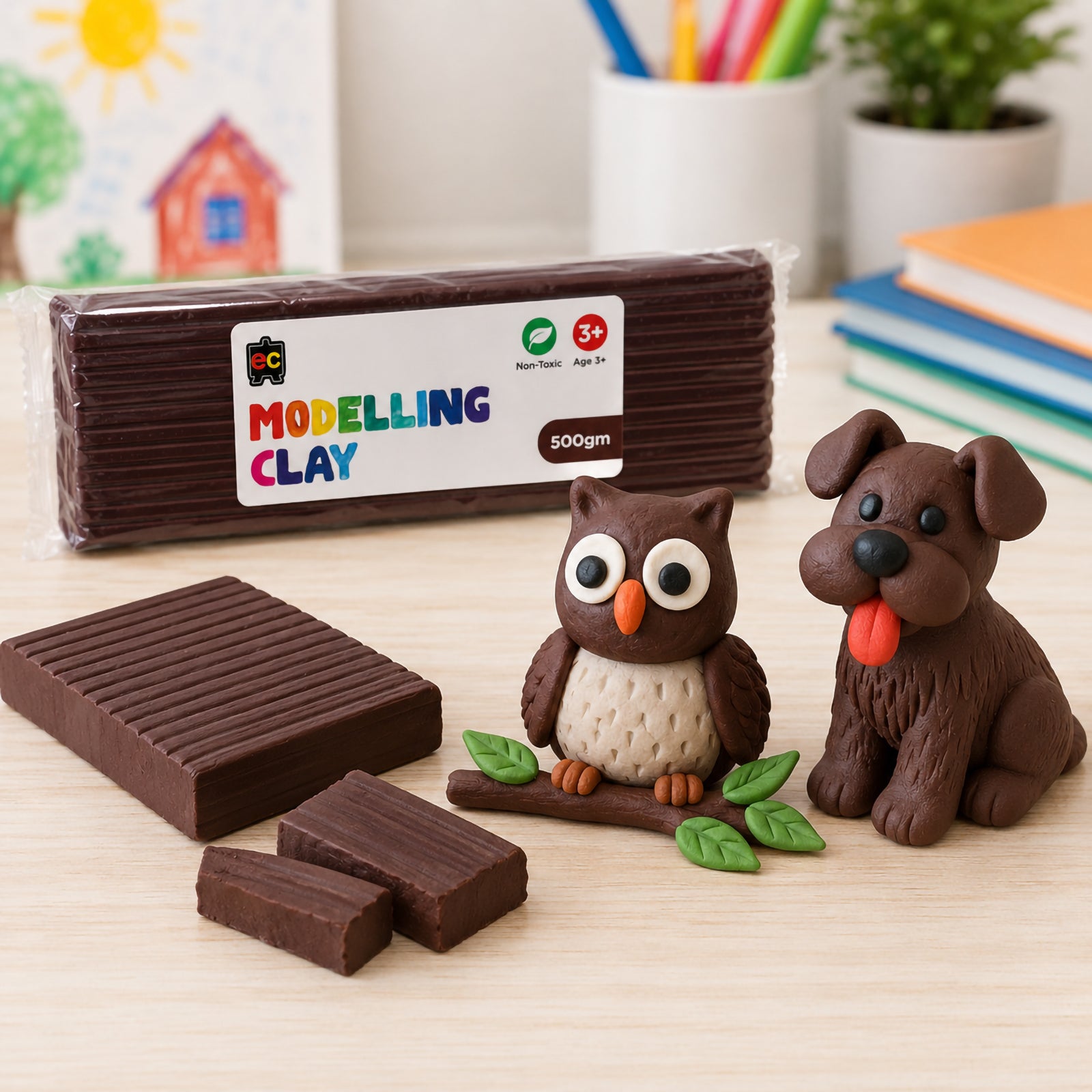 Educational Colours 500gm brown modelling clay displayed on a wooden craft table with handmade clay owl, dog, and leafy branch creations in a bright creative workspace.