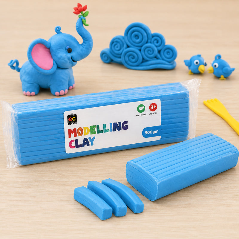 Light blue modelling clay block displayed on a wooden table with handmade clay elephant, spiral clay shapes, small blue birds and sculpting tools in a creative play setting.