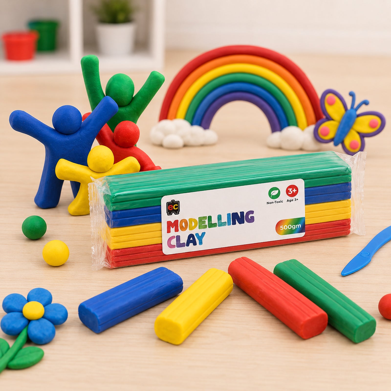 Pack of multicolour modelling clay surrounded by handmade clay figures, rainbow decorations, sculpting tools and bright clay pieces on a light wood tabletop.