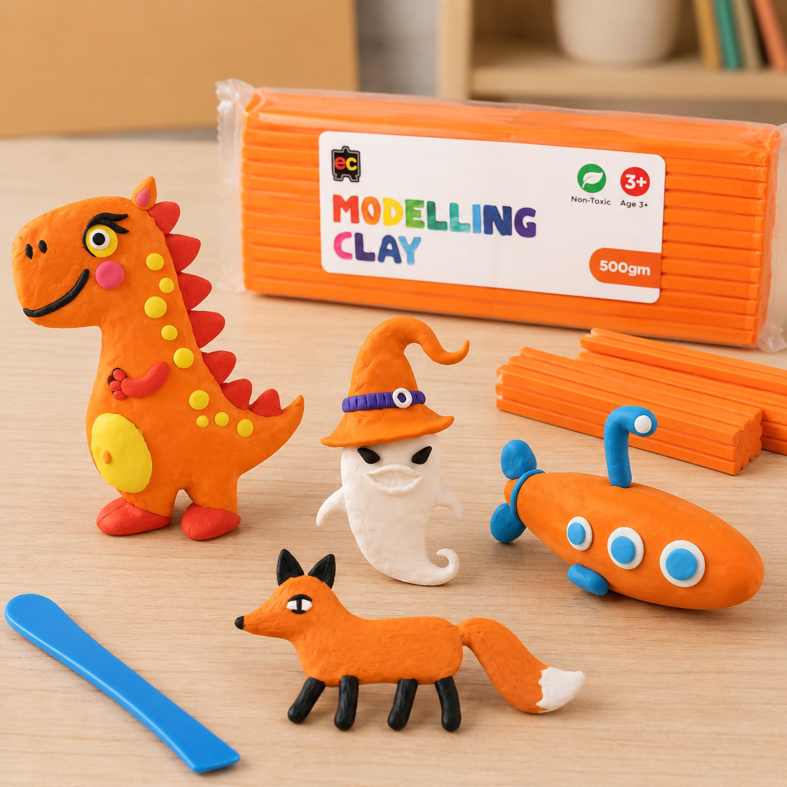 Educational Colours Modelling Clay 500g Orange displayed with handmade orange clay dinosaur, fox, ghost, and submarine figures on a bright wooden craft table.