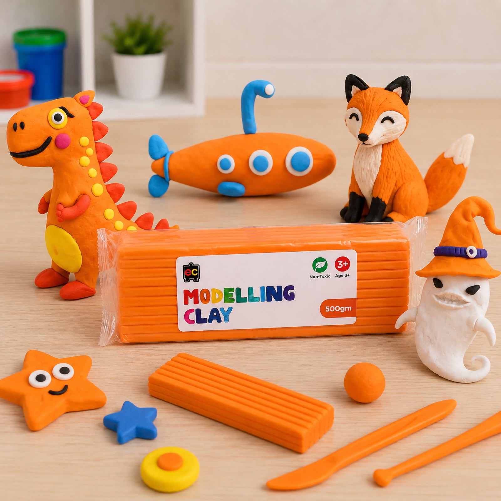 Educational Colours orange modelling clay pack displayed on a wooden craft table with handmade clay dinosaur, submarine, fox and ghost figures alongside sculpting tools and clay shapes.