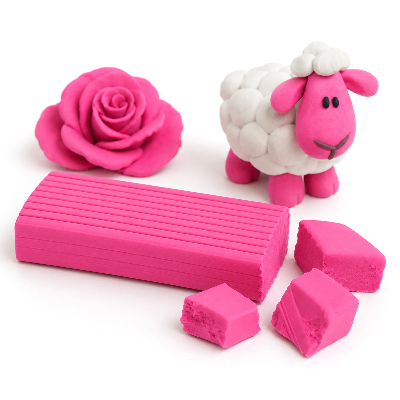 Close-up studio display of bright pink modelling clay with cut clay blocks beside a handcrafted pink rose and white sheep sculpture on a clean white background.