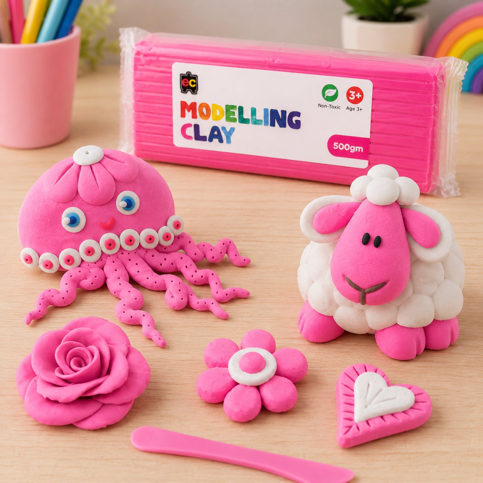 Educational Colours Modelling Clay 500g Pink displayed with handmade pink clay octopus, sheep, flower, rose, and heart shapes on a bright wooden craft table.