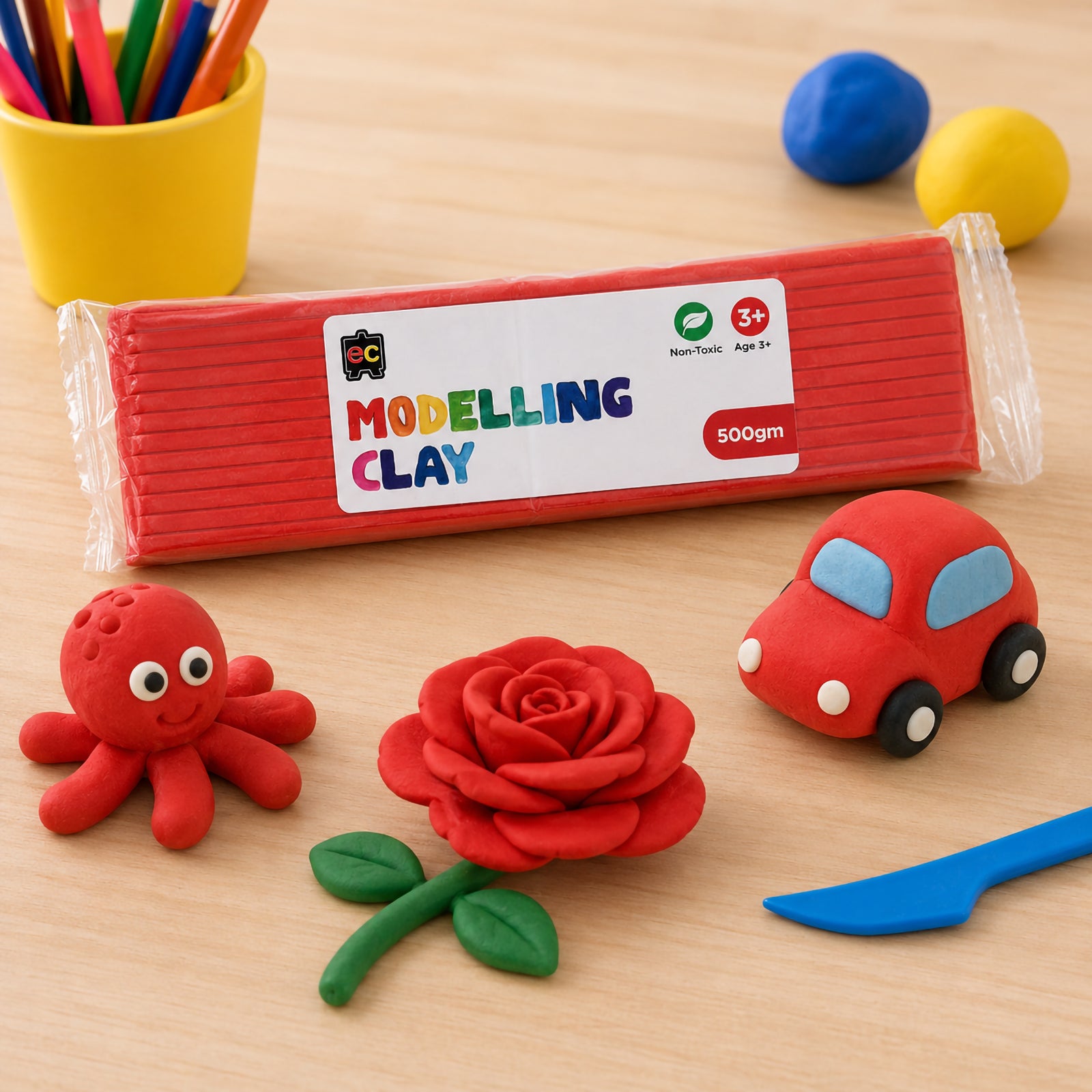 Educational Colours red modelling clay pack surrounded by colorful handmade clay crafts including a rose, toy car, and octopus on a bright wooden desk.