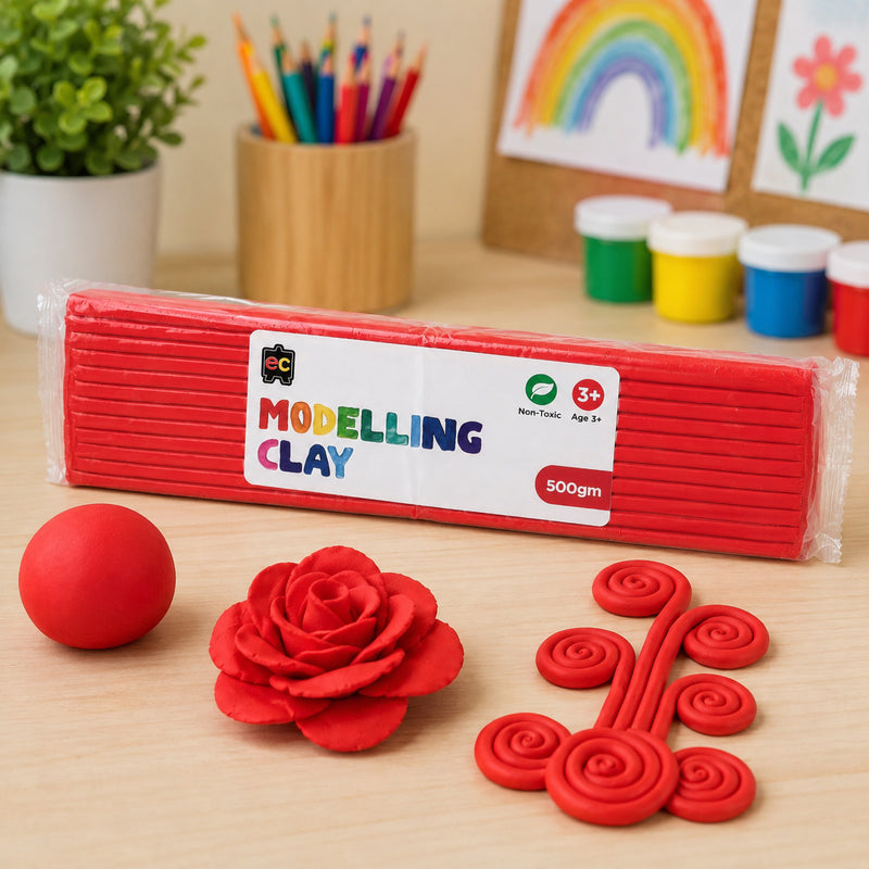 Educational Colours 500g red modelling clay pack on a classroom craft table with handmade clay rose shapes, spiral clay art, coloured pencils, and children’s artwork in the background.
