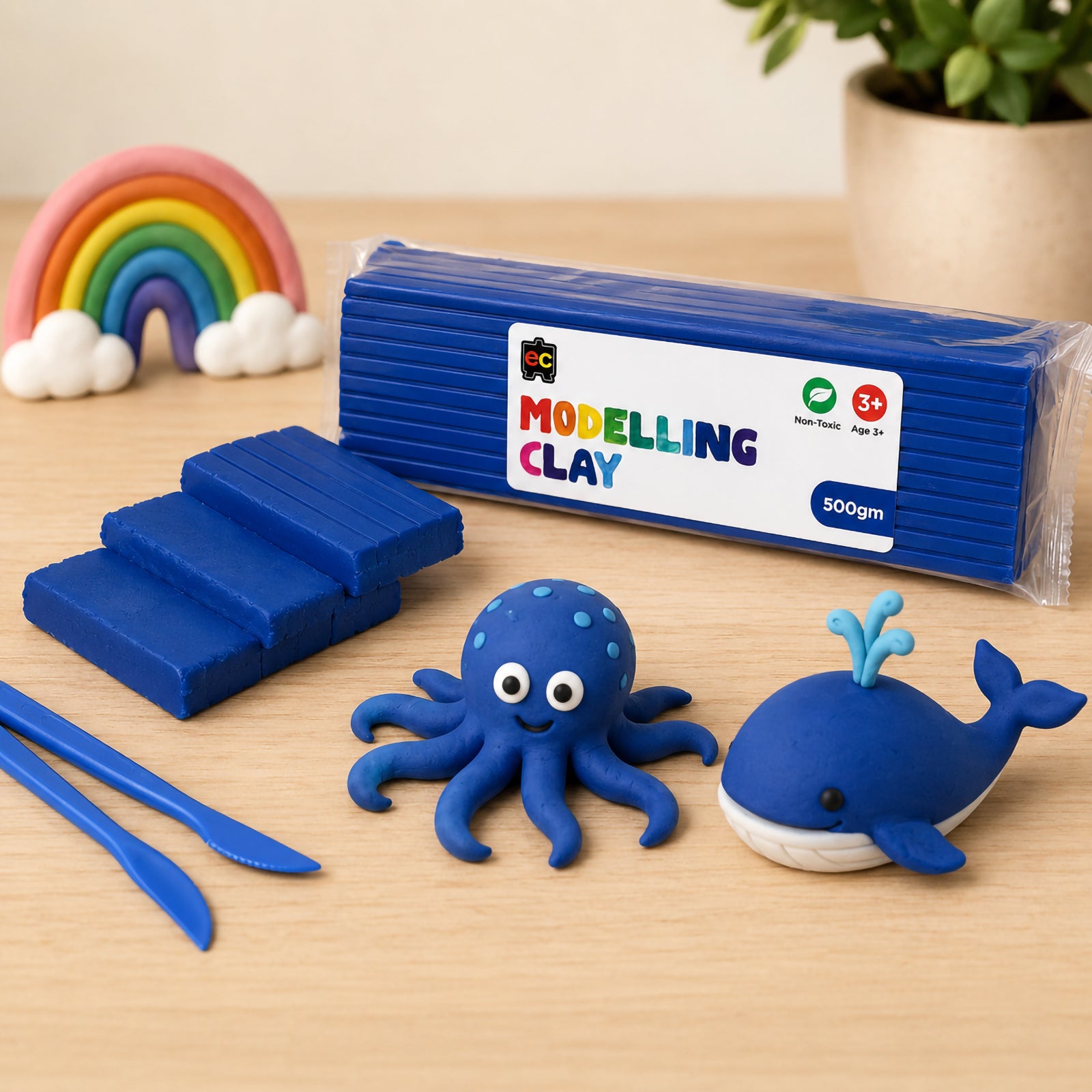 Educational Colours Modelling Clay 500gm Dark Blue displayed on a wooden tabletop with blue clay sea animal creations, sculpting tools, and rainbow decor in the background.
