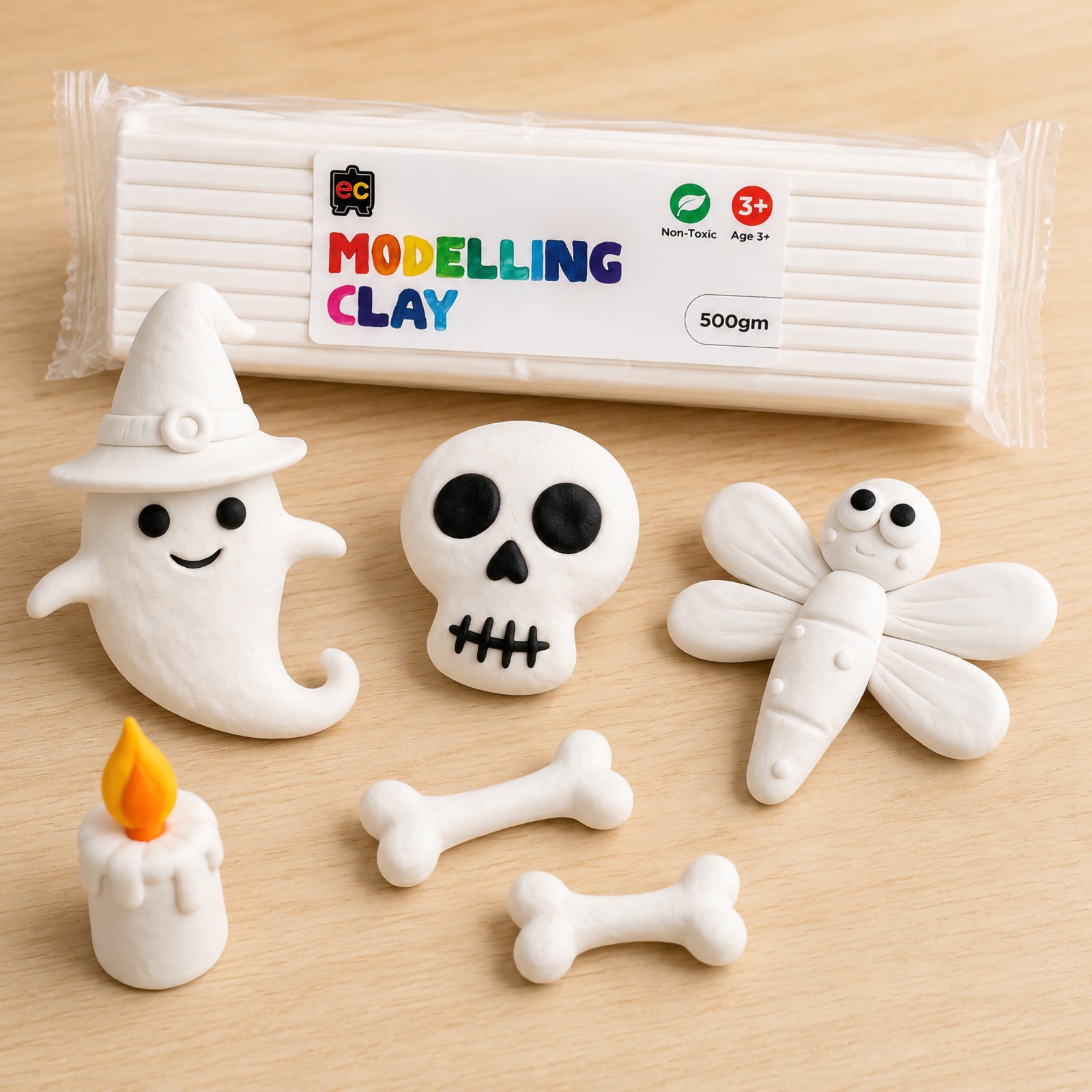 Packaged white modelling clay surrounded by detailed handmade clay Halloween figures including a ghost, skull, bones, and dragonfly in a bright studio setting.