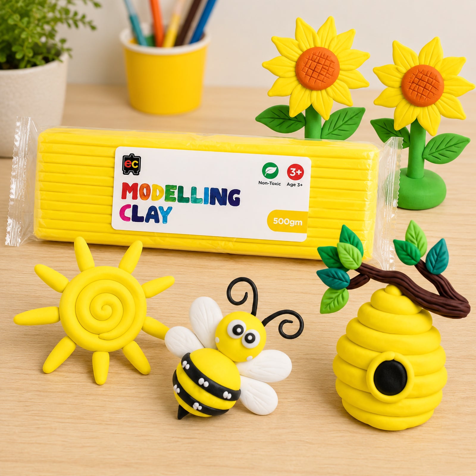 Educational Colours yellow modelling clay pack with detailed handmade clay sunflowers, bee, beehive, and sun arranged on a light wood craft table.
