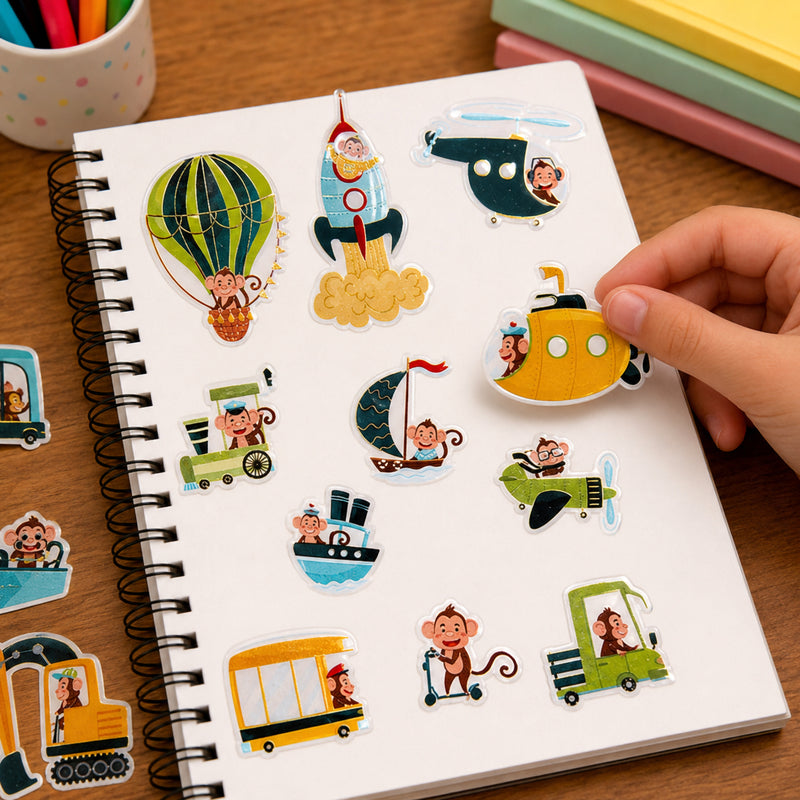 Child placing a bright yellow submarine sticker onto a notebook page filled with adventurous monkey characters travelling by rocket, helicopter, hot air balloon and boat. The foil accents add a reflective shimmer while encouraging imaginative travel themed storytelling.