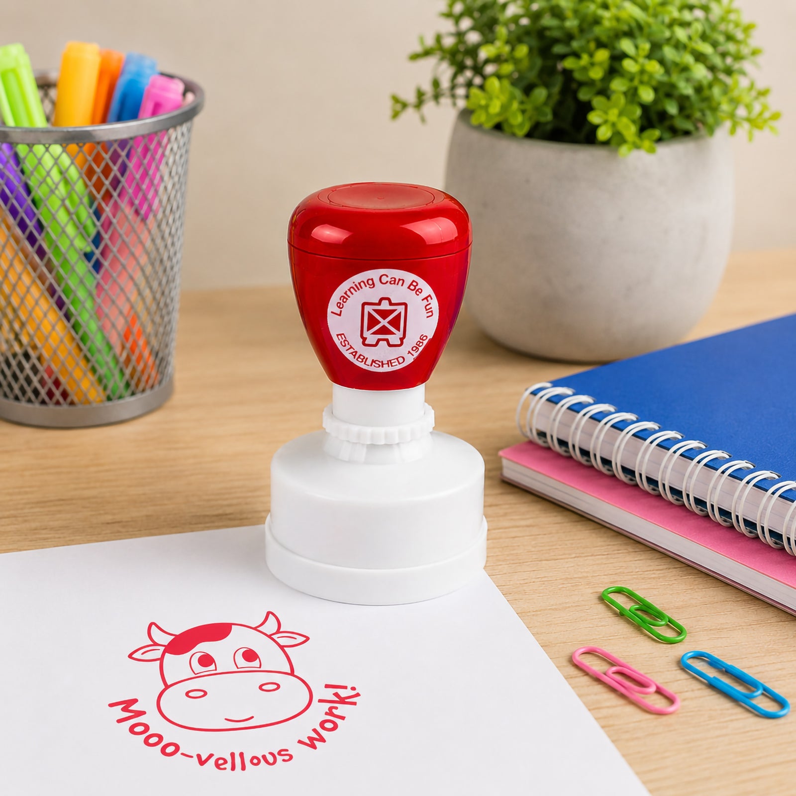 Self inking Mooo vellous Work reward stamp positioned beside notebooks, paper clips and classroom supplies. The playful cow design creates engaging and encouraging feedback for students of all ages.