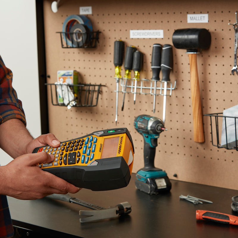 Person holding a handheld device in front of a pegboard with tools