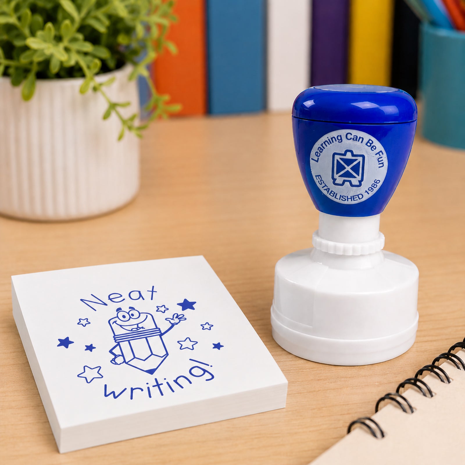 Close up classroom scene featuring the Neat Writing Merit Stamp next to a notepad and educational resources. The bold blue impression highlights positive reinforcement for students who take care with their writing.