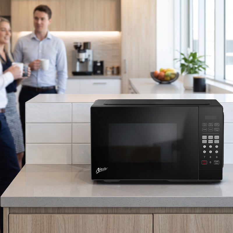 Nero 25L black microwave on an office kitchen bench with a mug beside it and staff talking in the background