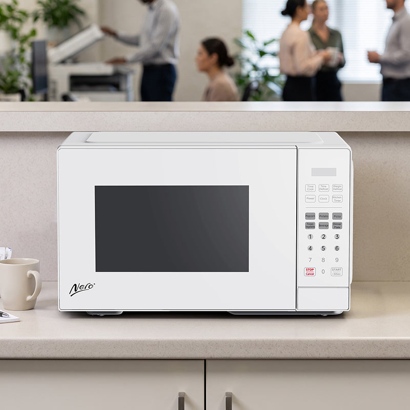 Nero 25L white microwave on an office kitchen bench with a mug beside it and staff talking in the background