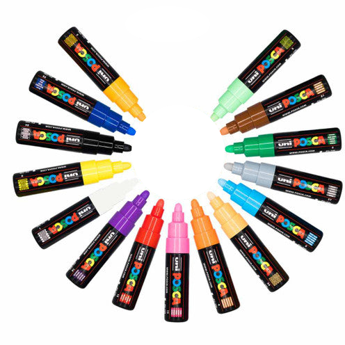 15 Uni Posca paint markers arranged in a circular pattern on a white background, showing a variety of colours including yellow, blue, green, brown, grey, light blue, purple, red, pink, orange, and beige.
