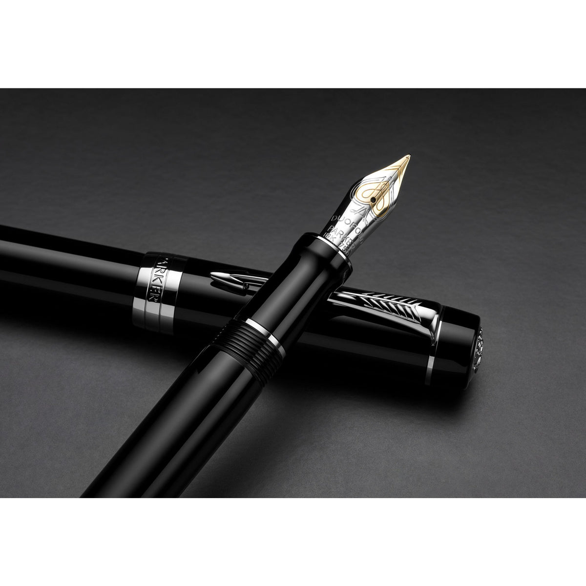 Black Duofold fountain pen with silver-tone trims lying over its cap on a dark background, two-tone gold nib facing up