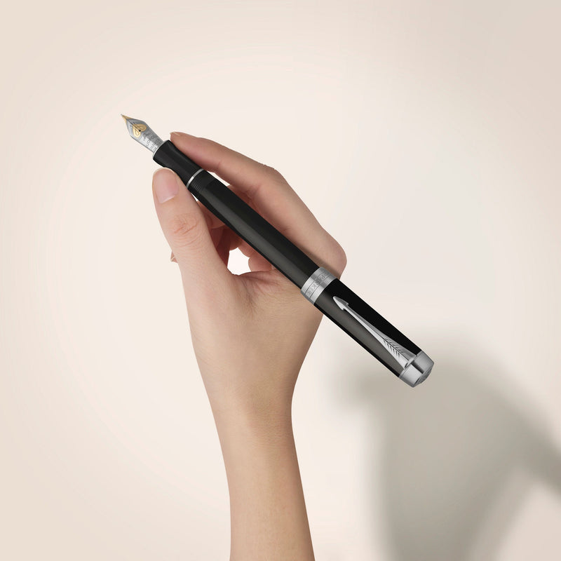 A hand holding the black Duofold Classic fountain pen with palladium trims against a pale wall