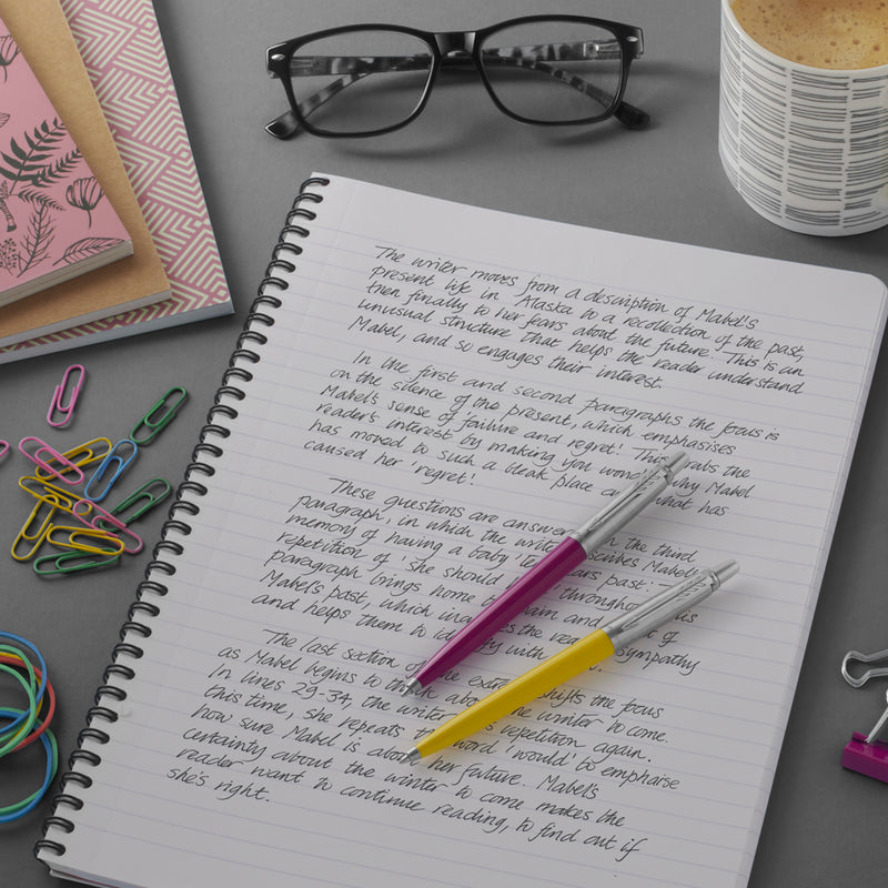 Pink and yellow Parker Jotter pens resting on a spiral notebook filled with dark handwriting