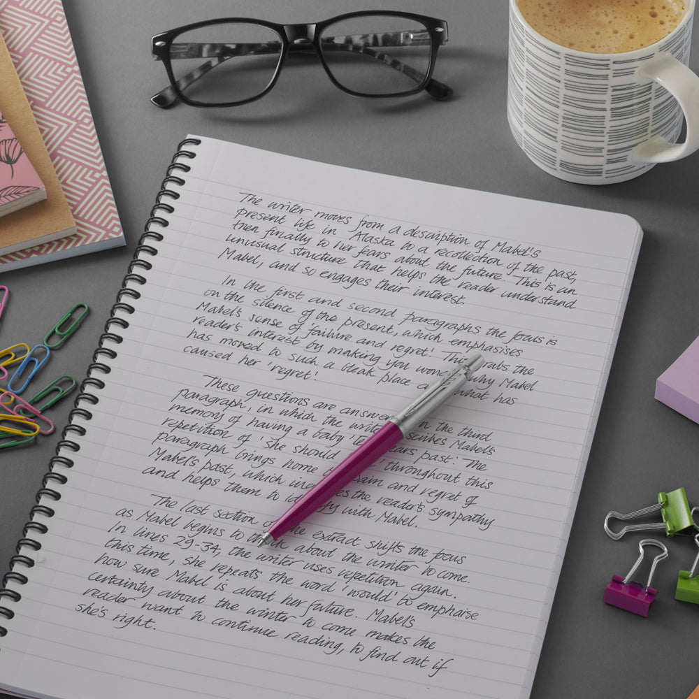 Pink Parker Jotter on a handwritten notebook page next to glasses, a mug and paper clips
