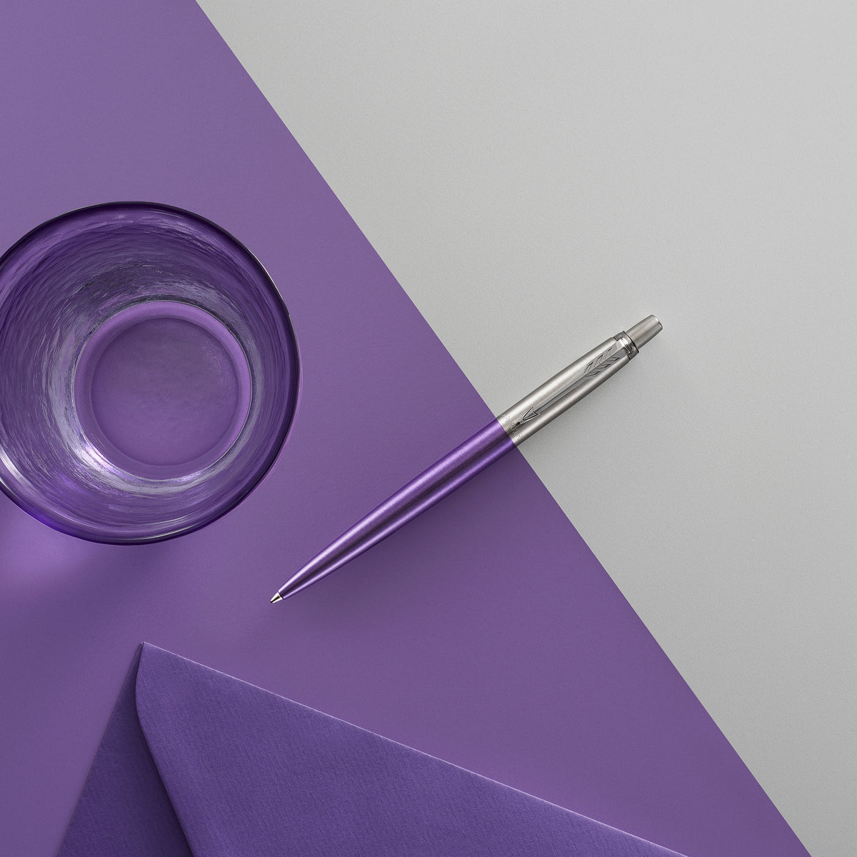 Violet Jotter ballpoint resting on a grey and purple surface beside a glass and a lilac envelope