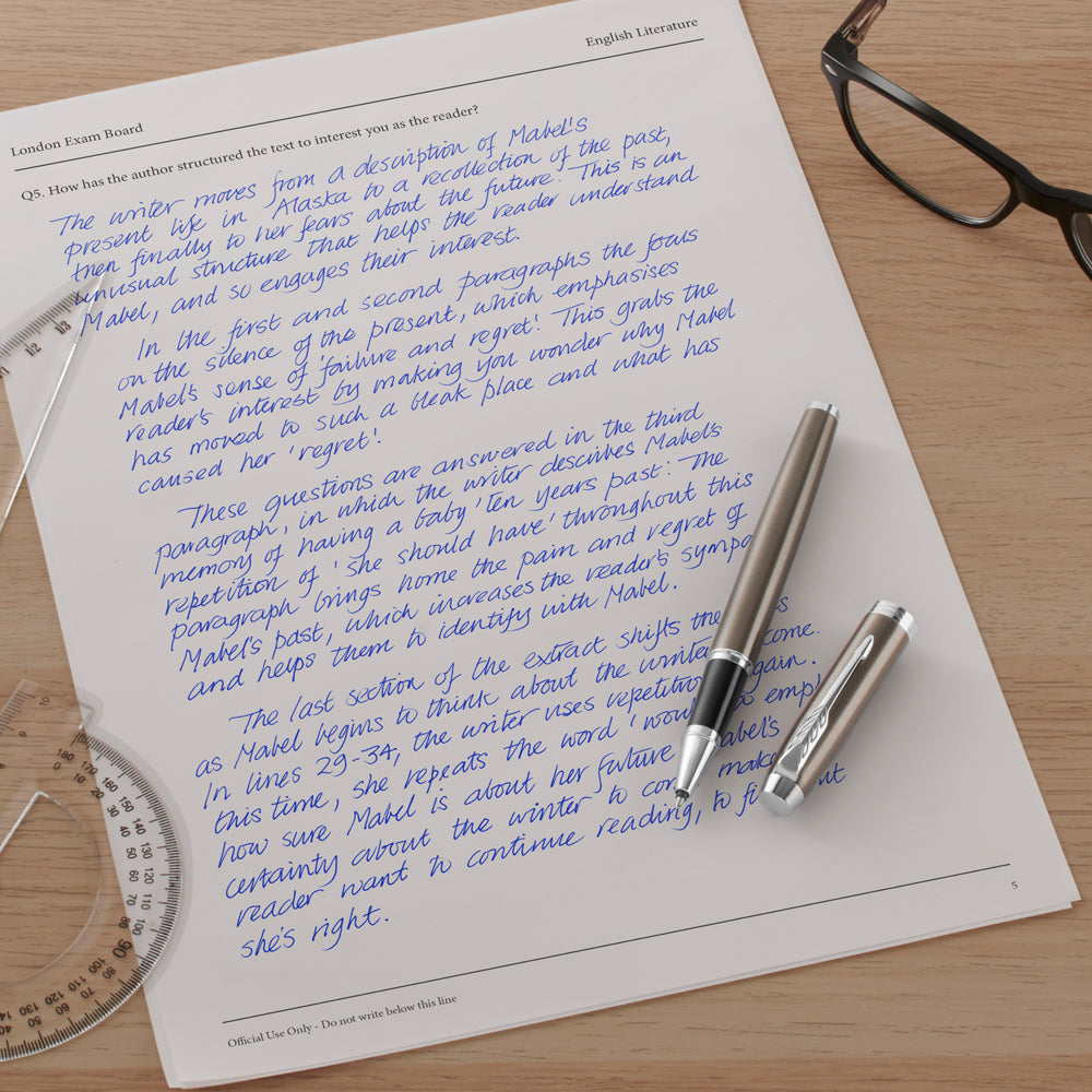 Blue handwritten essay page with a grey Parker rollerball and its cap, protractor and glasses nearby