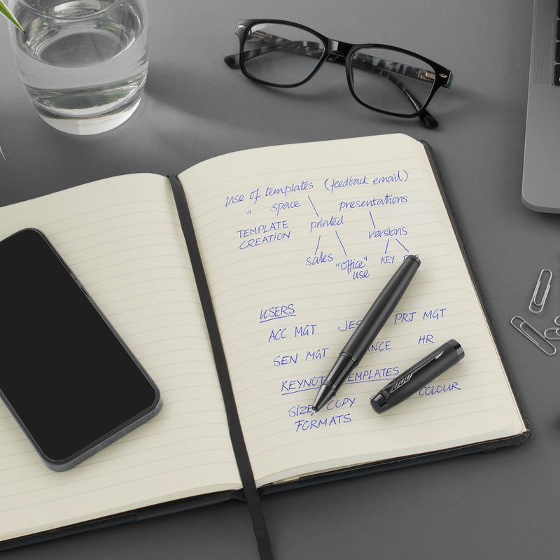Black Parker pen on an open notebook with blue handwritten notes, a phone, glasses and a glass of water