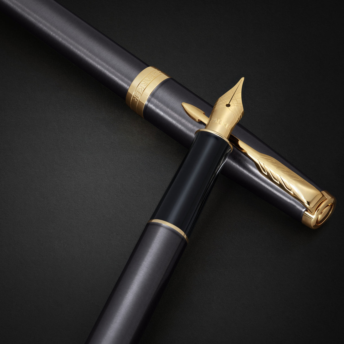 Grey Sonnet fountain pen crossed over its cap on a dark background, gold nib facing up