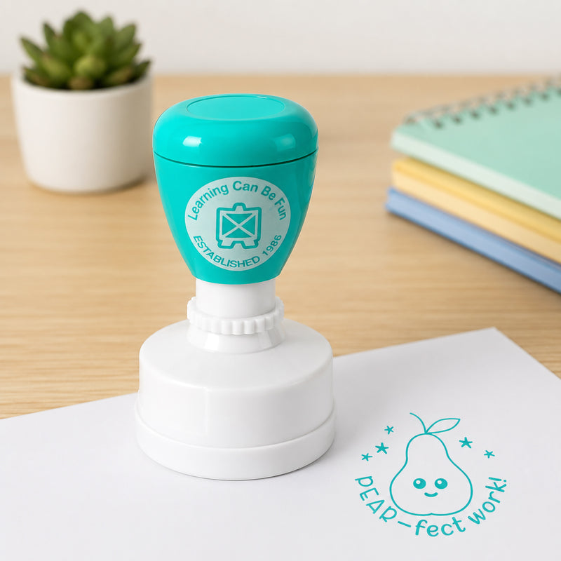 Pear-fect Work merit stamp shown on a worksheet with colourful notebooks in the background. The bright teal impression provides clear recognition for outstanding classroom performance, helping students feel valued and encouraged.