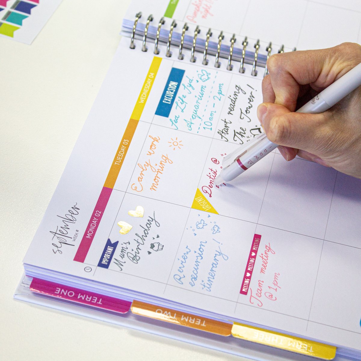 A Pilot FriXion Waai gel pen erasing handwriting in a planner, demonstrating the erasable ink.