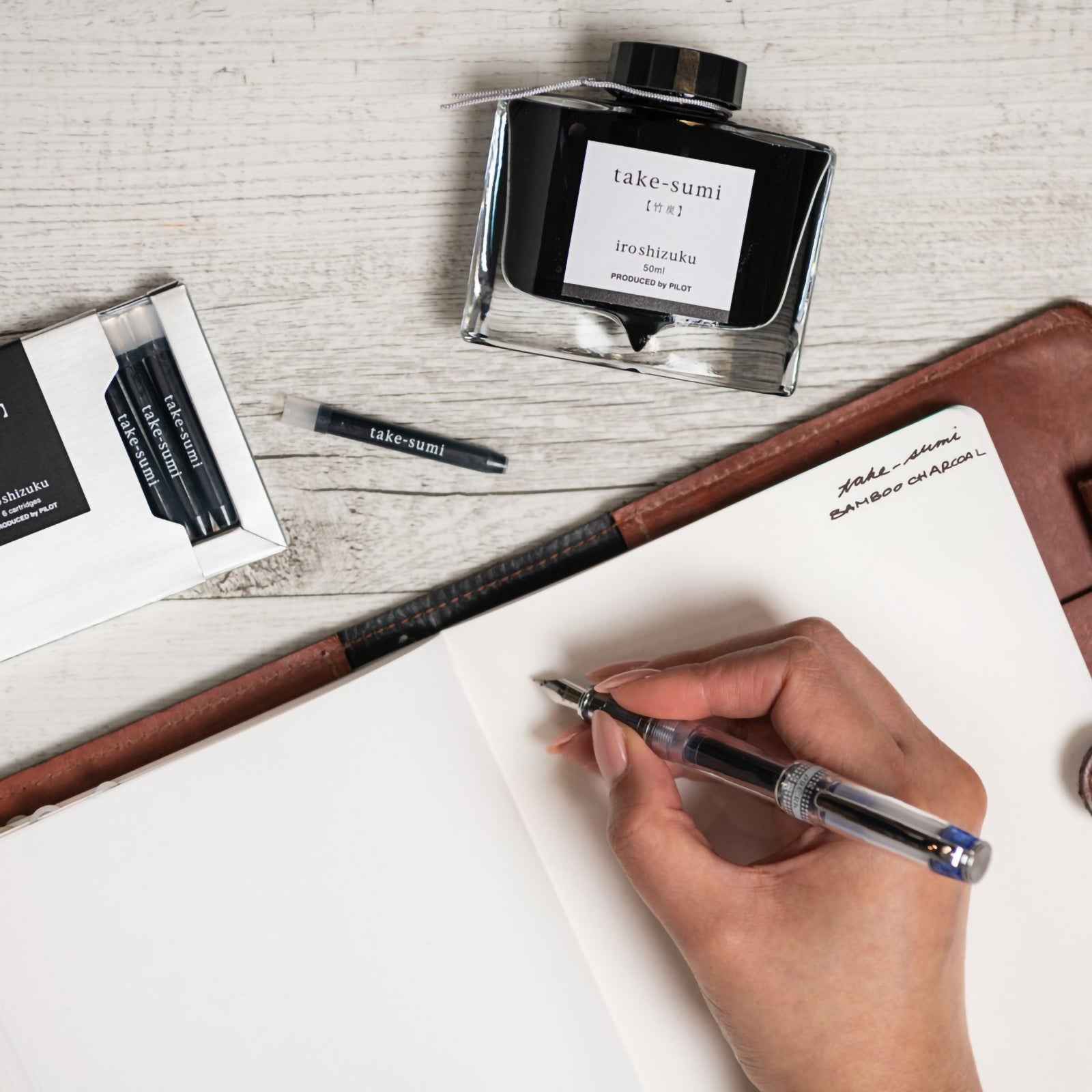 Creative writing workspace featuring the Pilot Iroshizuku Take Sumi cartridge box, matching 50ml ink bottle, loose cartridge and compatible fountain pen beside an open notebook. The scene reflects the calm elegance and precision of Japanese writing culture.