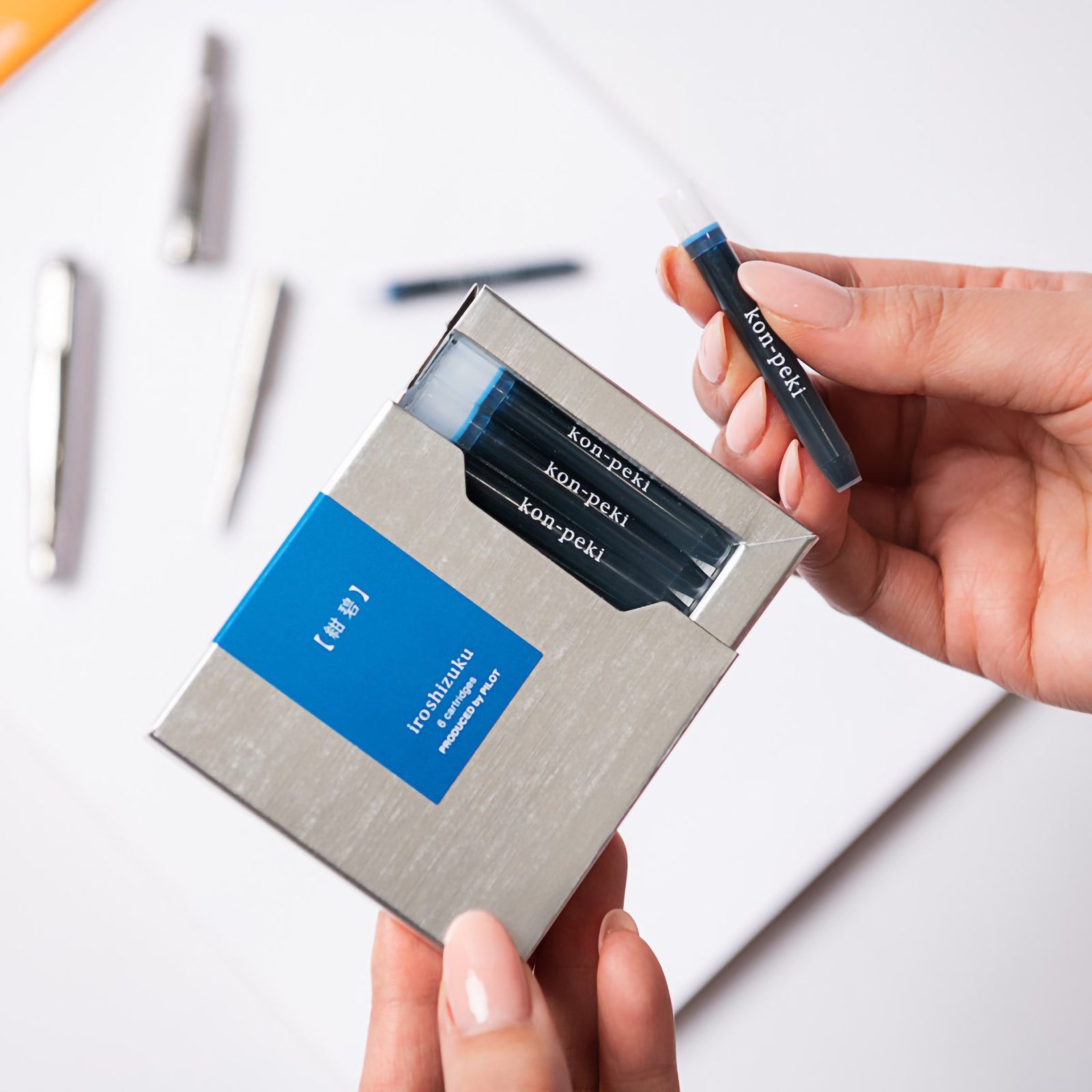A hand removes a Pilot Iroshizuku Kon Peki fountain pen ink cartridge from the premium six cartridge presentation box, demonstrating the convenient proprietary cartridge design for quick and clean fountain pen refilling.