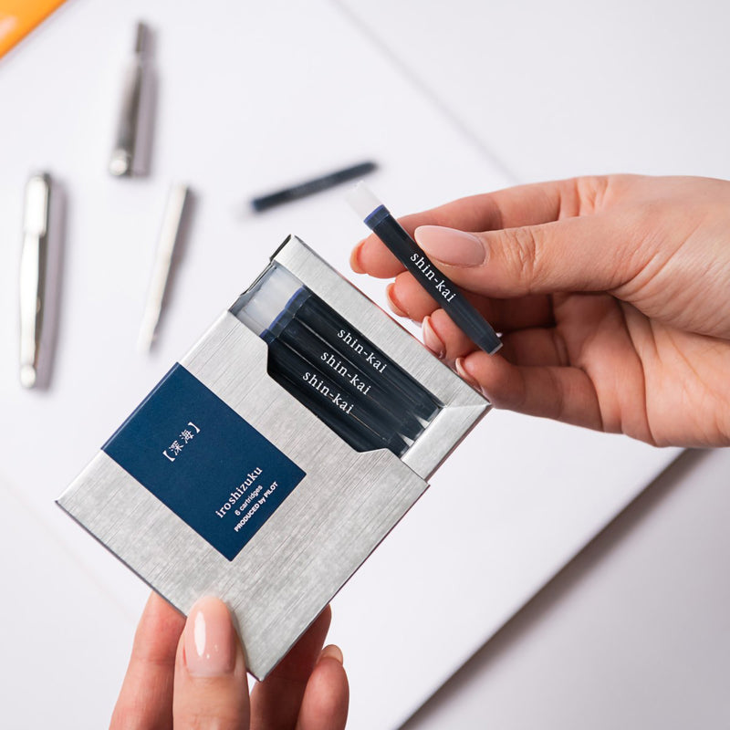 A hand removes a genuine Pilot Iroshizuku Shin Kai fountain pen ink cartridge from the premium six cartridge presentation box, demonstrating the convenient proprietary cartridge system for quick and clean fountain pen refilling.