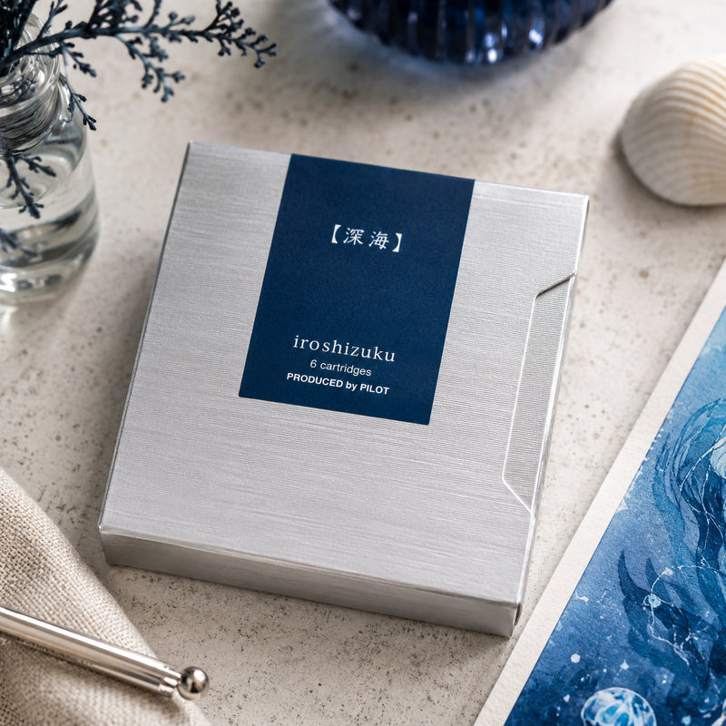 Pilot Iroshizuku Shin Kai fountain pen ink cartridge presentation box displayed on a stylish workspace with coastal inspired accessories, blue artwork and elegant desktop items. The composition reflects the calm depth and sophistication behind the Deep Sea ink colour.