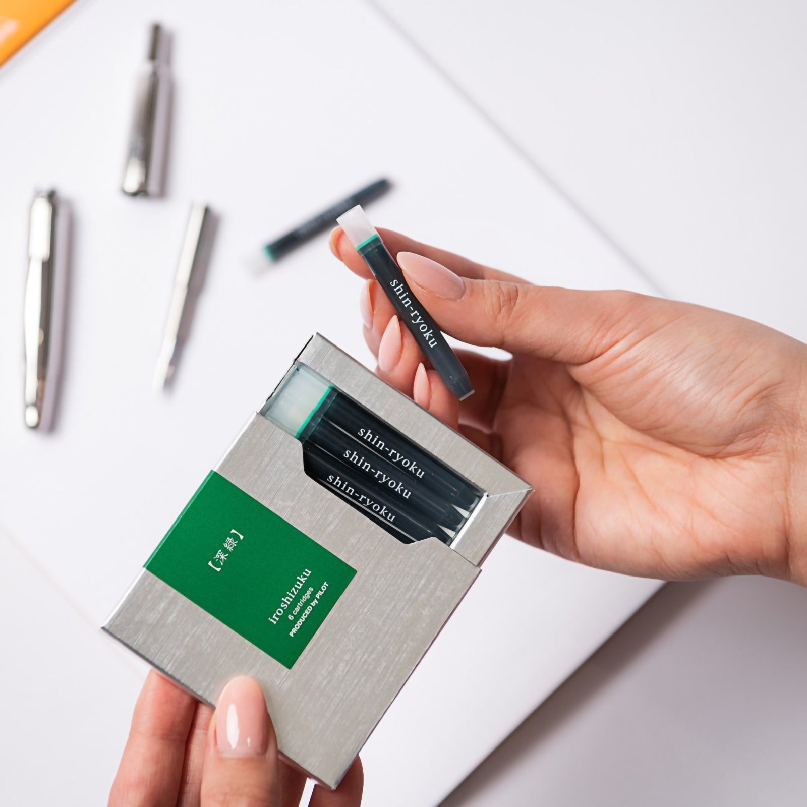 A hand removes a genuine Pilot Iroshizuku Shin Ryoku fountain pen ink cartridge from the premium six cartridge presentation box, highlighting the convenient proprietary cartridge system for clean and effortless fountain pen refilling.