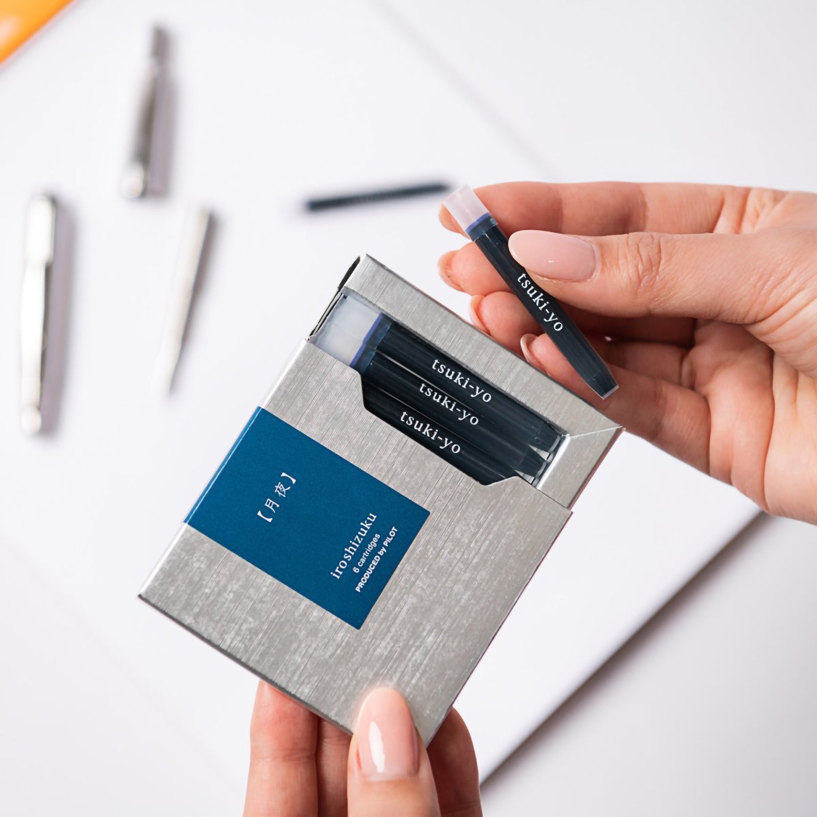 A hand removes a genuine Pilot Iroshizuku Tsuki yo fountain pen ink cartridge from the premium six cartridge presentation box, demonstrating the convenient proprietary cartridge system for quick and clean fountain pen refilling.