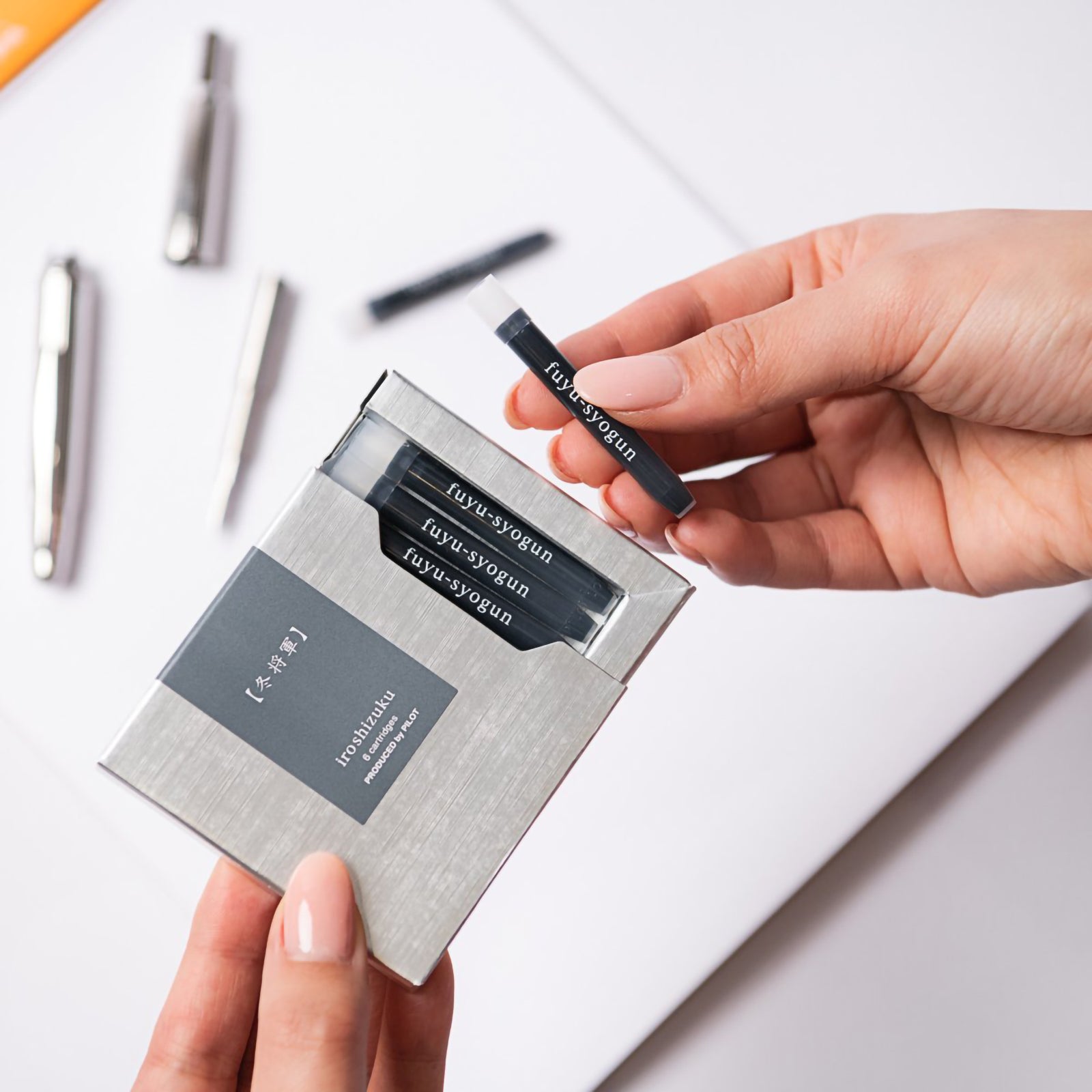 A hand removes a genuine Pilot Iroshizuku Fuyu syogun fountain pen ink cartridge from the premium six cartridge presentation box, highlighting the convenient proprietary cartridge design for quick and clean fountain pen refilling.