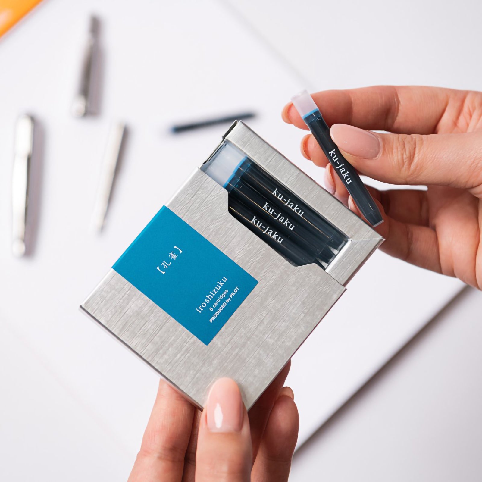 A hand removes a genuine Pilot Iroshizuku Ku jaku fountain pen ink cartridge from the premium six cartridge presentation box, highlighting the convenient proprietary cartridge design for quick and clean fountain pen refilling.