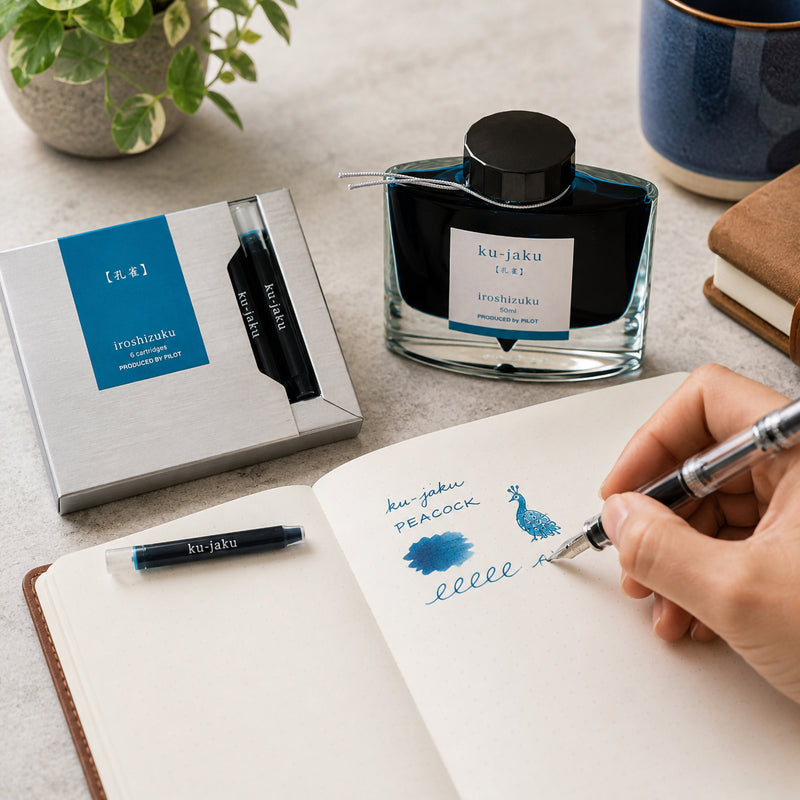 Pilot Iroshizuku Ku jaku Peacock fountain pen ink cartridges displayed beside the matching 50ml ink bottle while a hand writes and sketches colour samples in an open notebook. The vibrant blue green ink highlights the inspiration drawn from the brilliant feathers of the peacock.