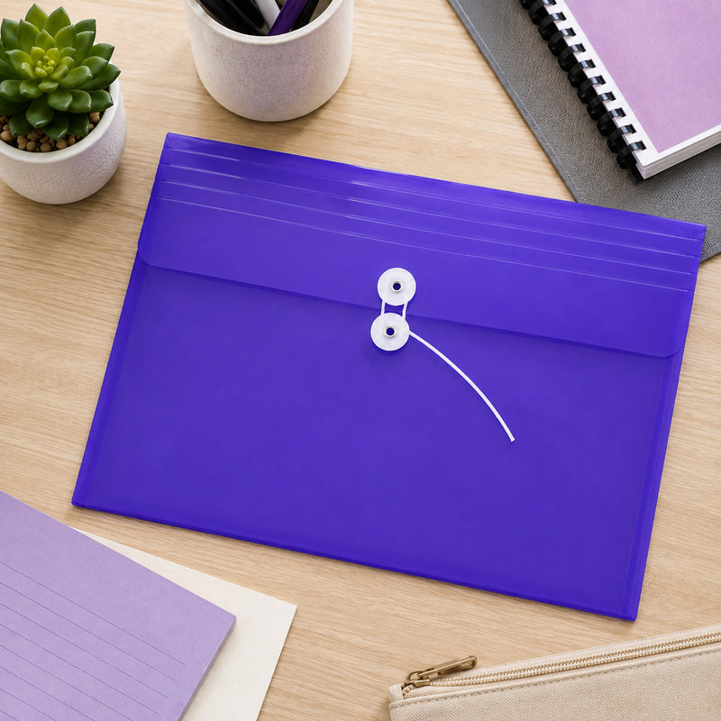 Pop purple foolscap document wallet resting flat on a timber desktop alongside stationery, notebooks and small plants. The translucent purple envelope has a landscape profile with a white string closure positioned centrally on the flap. This overhead view highlights the broad storage format and distinctive colour for organising paperwork, projects, study notes or office documents.