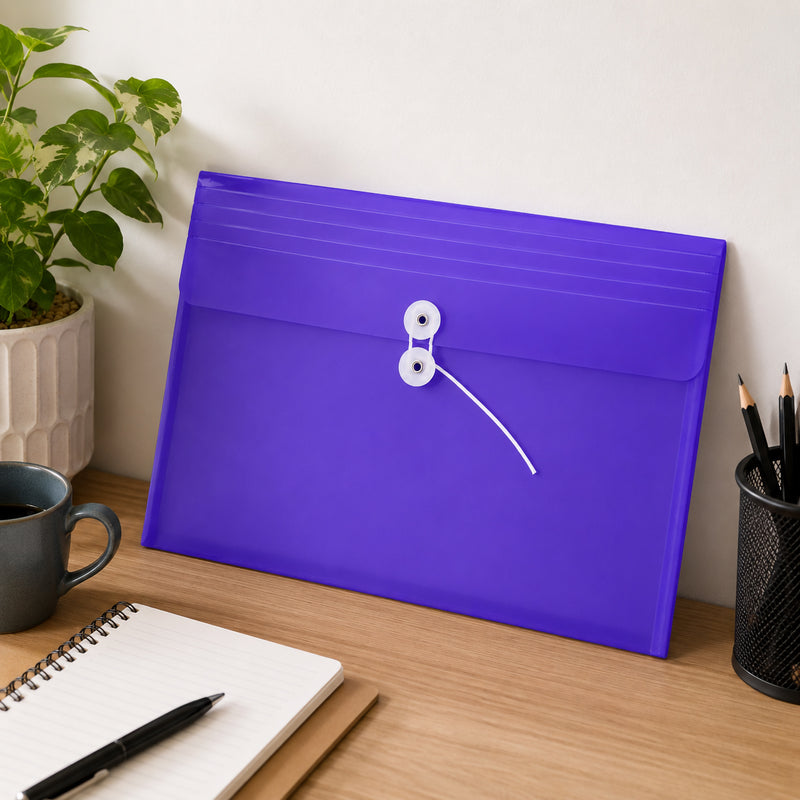 Purple Pop Polywally foolscap wallet displayed upright on a workspace beside a notebook, coffee cup, plant and pencil holder. The translucent envelope body, landscape flap and white button and string fastening are clearly visible. The vibrant purple finish provides an easy visual reference for colour coded filing while keeping loose documents neatly contained.
