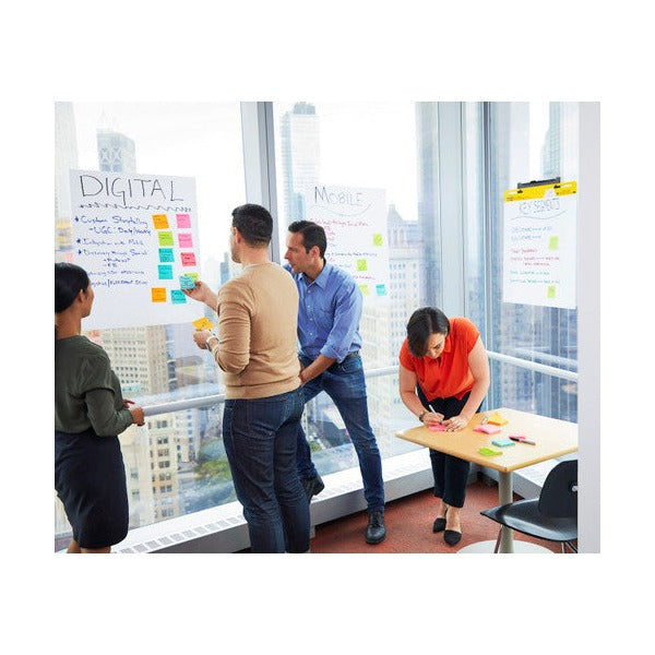 Colleagues adding sticky notes to an easel sheet stuck to an office window, with notes on a table nearby