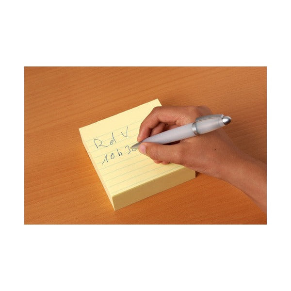 Hand writing a short note on a lined canary yellow Post-it pad resting on a timber desk