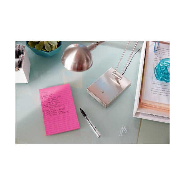 Pink lined note with handwritten notes on a glass desk beside a silver desk lamp and a pen
