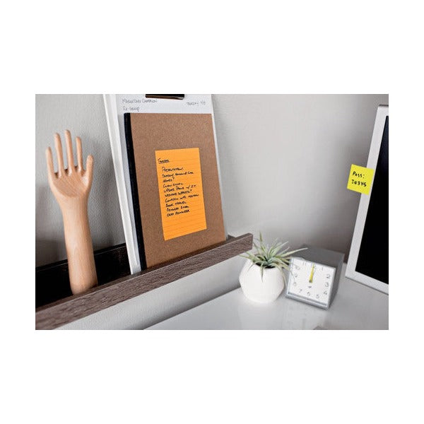 Orange lined note with a handwritten list pinned to a kraft board on a shelf beside a wooden hand model and desk clock