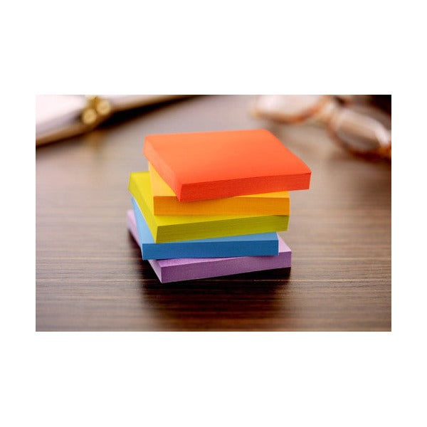 Stack of square Post-it notes in red-orange, yellow, green, blue and purple on a wooden table with glasses behind