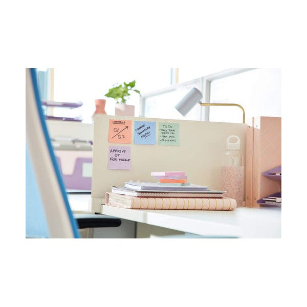 Office desk partition with pastel notes stuck to it, handwritten with tasks, beside a lamp, a plant and a stack of books